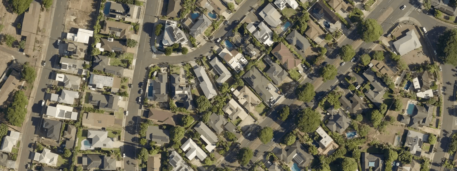 Aerial imagery of an Oʻahu neighbourhood at close range: individual houses, driveways, pools, garden beds and street trees are separately legible.